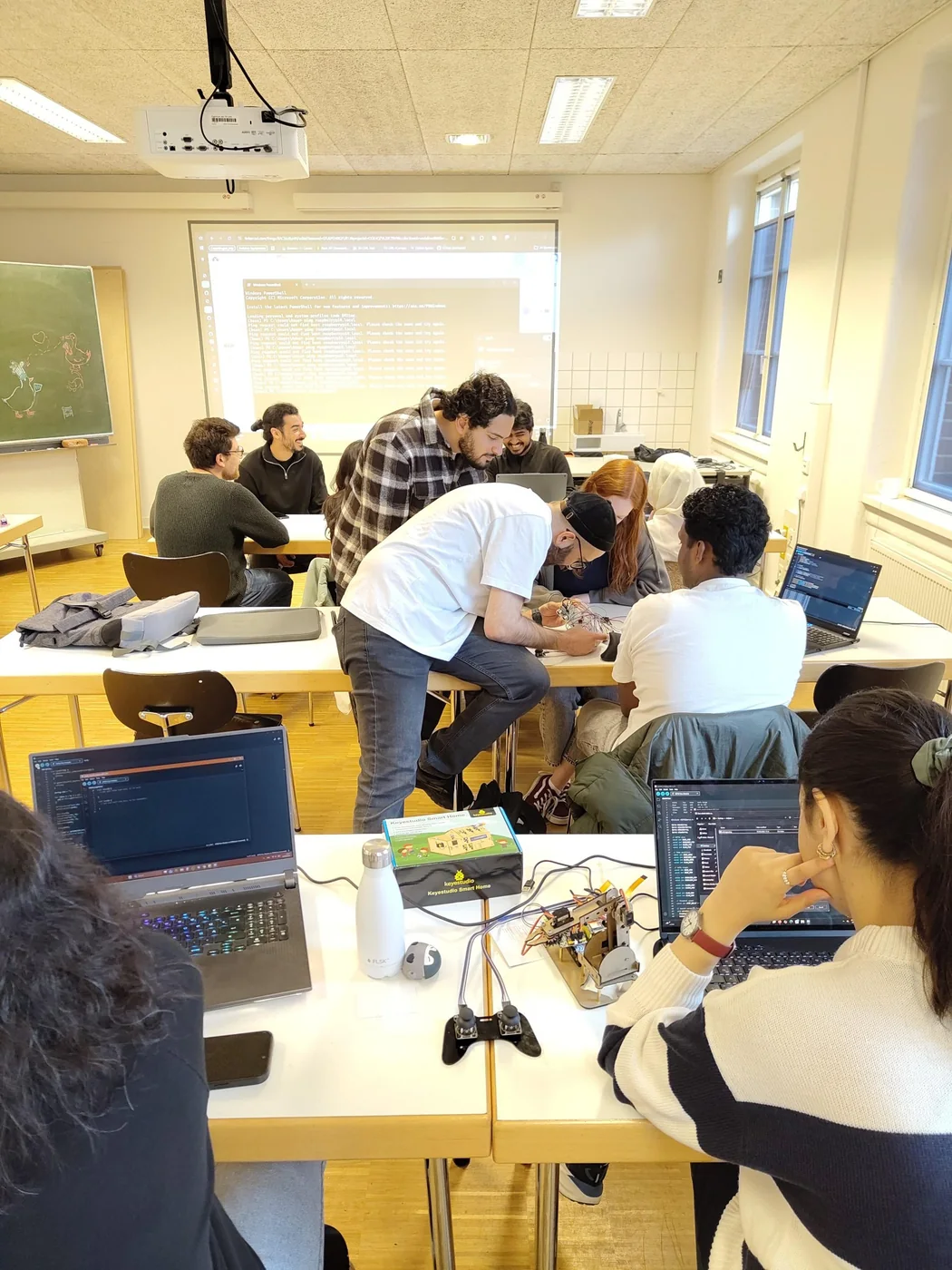 Students working at laptops with robot kits and cables spread across studio tables