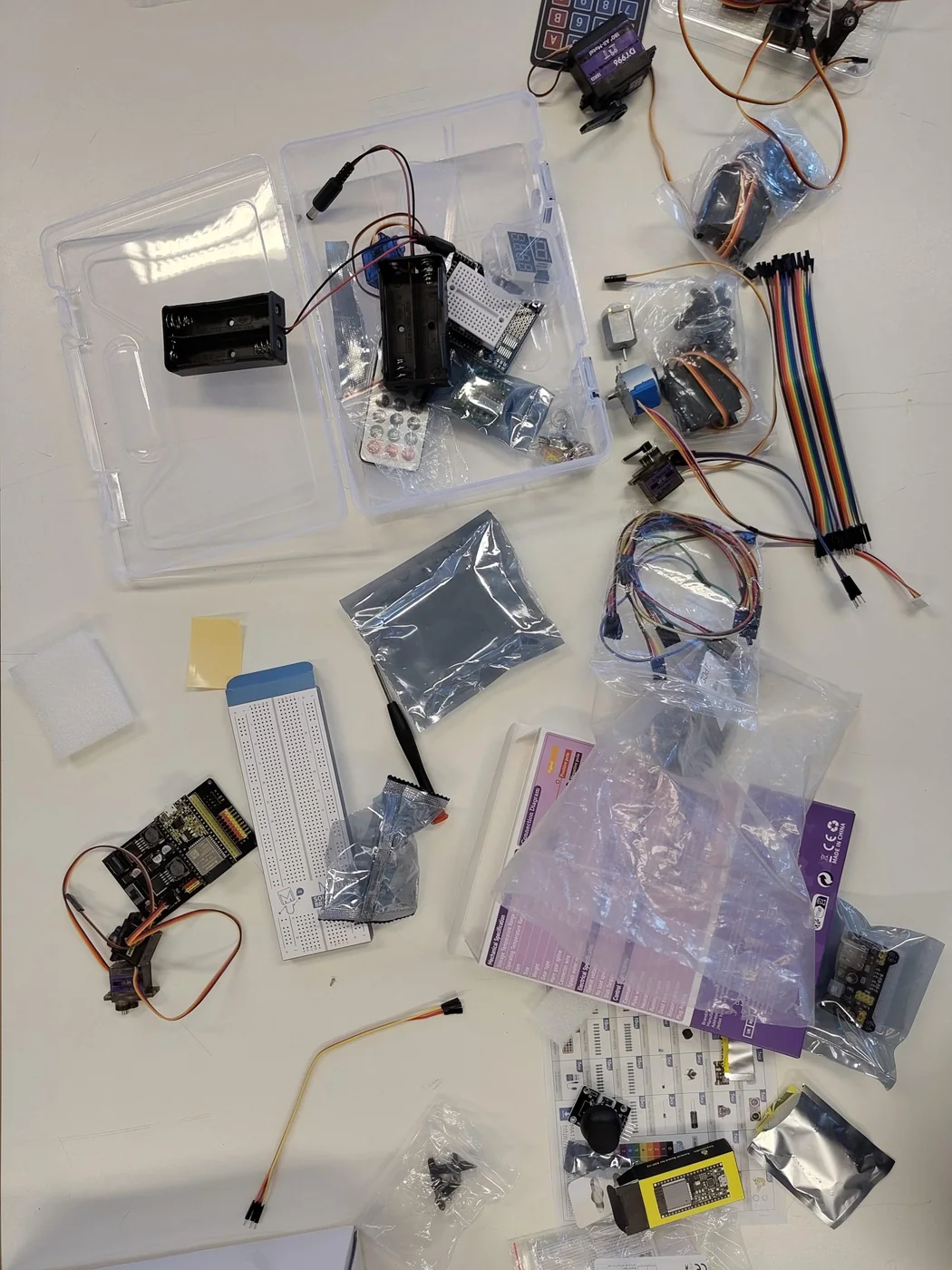 Open-source robotics kit laid out on a table: microcontroller boards, servos, jumper wires, battery packs and sensors in bags