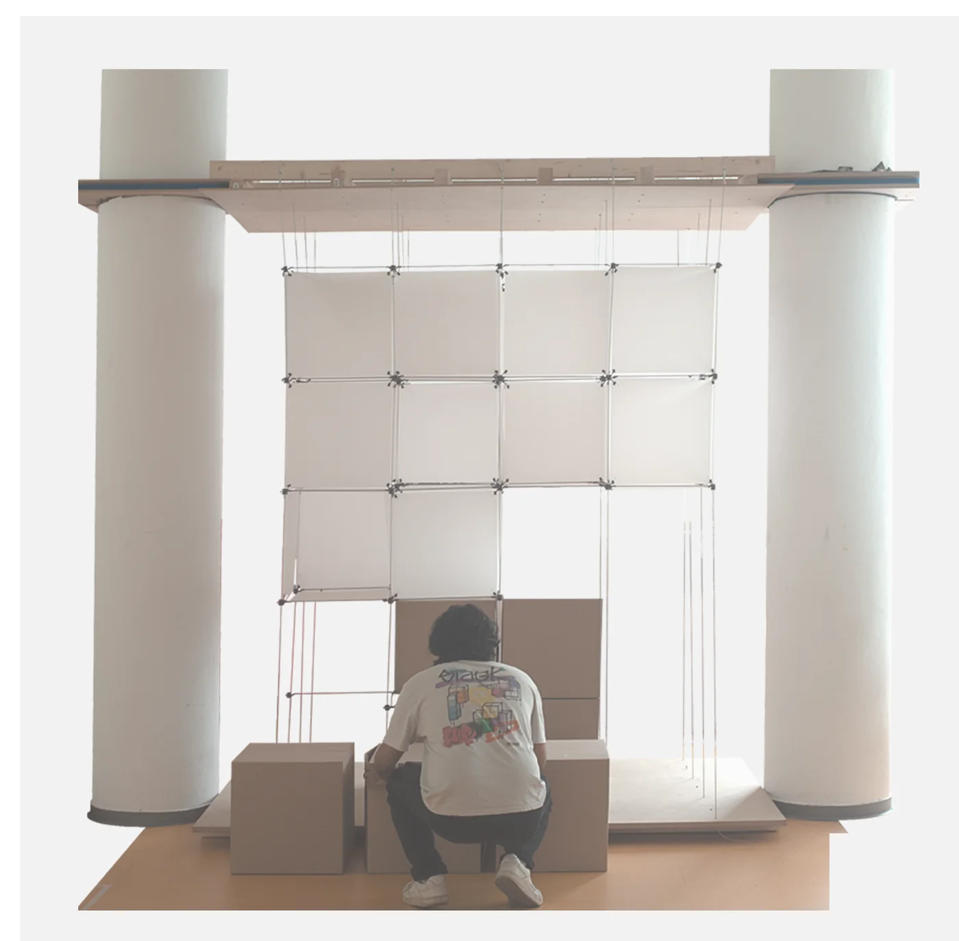 The physical voxel installation: a suspended grid of panels between two columns with a person seated inside